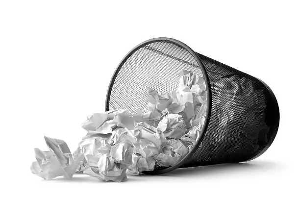 A metal wastebasket tipped over, spilling crumpled paper